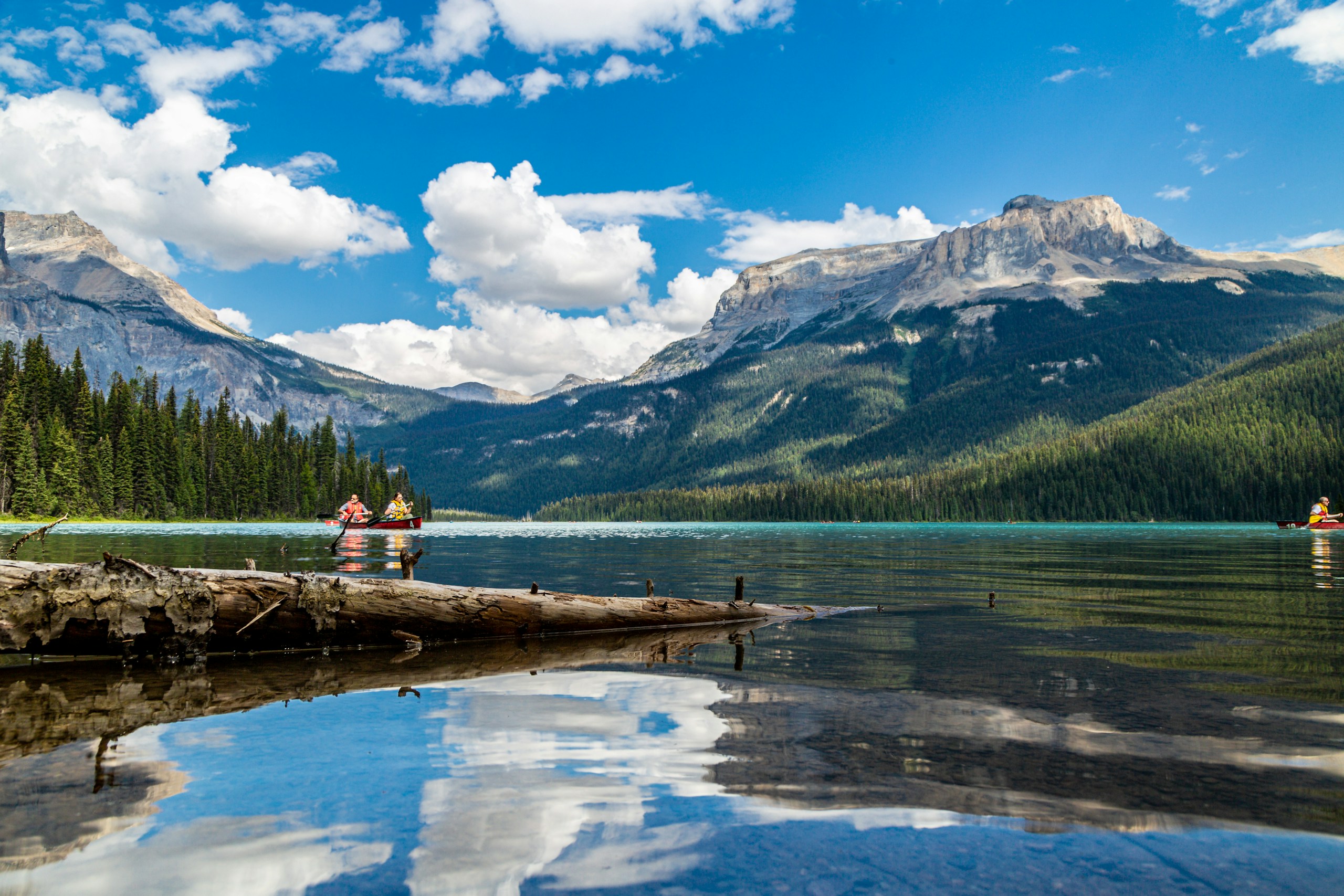 a group of people on a log in a lake with mountains in the background
