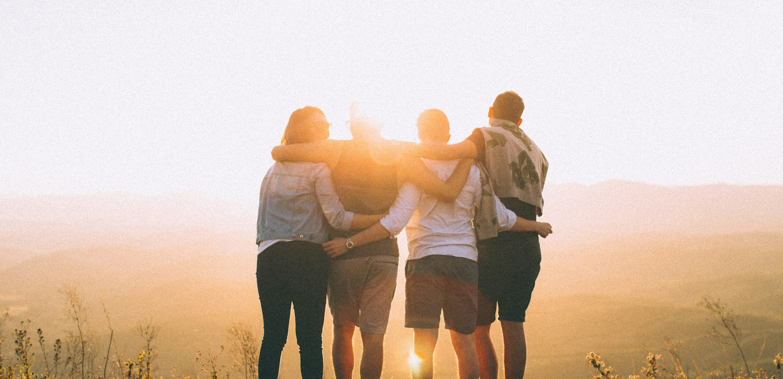 four person hands wrap around shoulders while looking at sunset