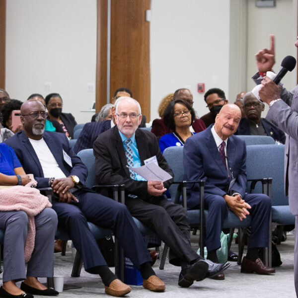 A Black man preaches in front of a diverse crowd of men and women