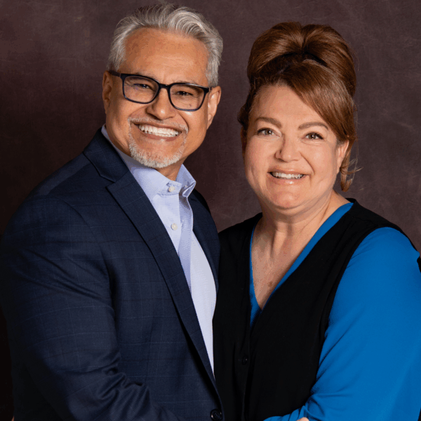 A smiling Hispanic couple pose for a formal photo with arms around each other