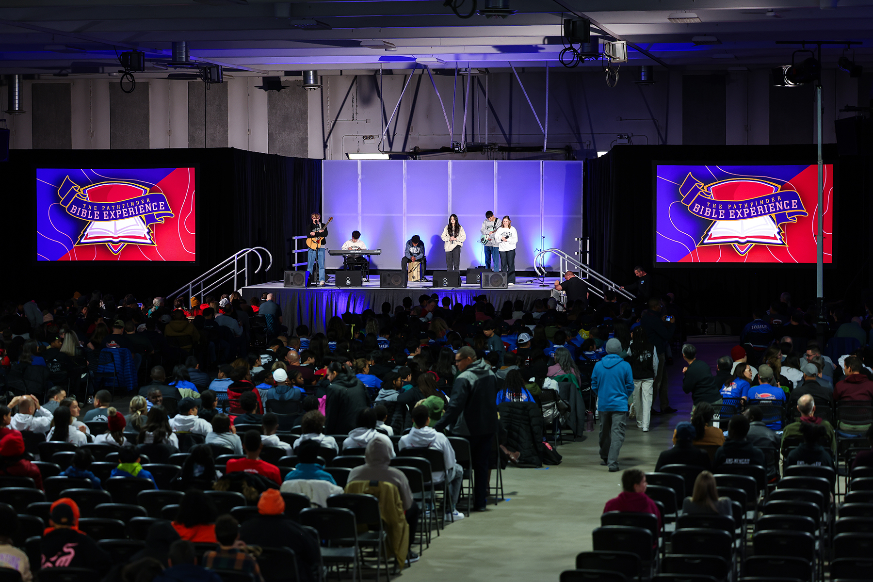 An auditorium full of people with a praise team in the front, in the distance.