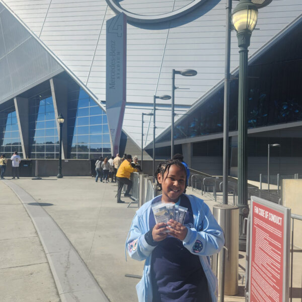 A smiling young girl holds several tracts in front of the Mercedes Stadium in Atlanta.