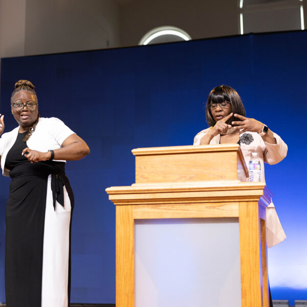 A woman interprets a presentation of another woman speaking behind a podium