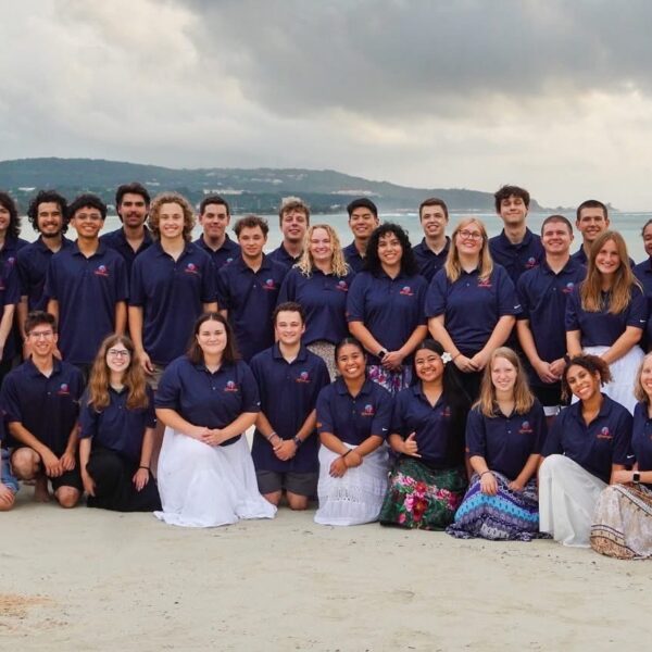 Large group of people posing on a beach in organized rows for a group photo.