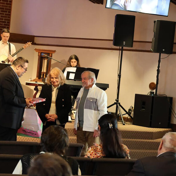 A pastor gives a gift to an elderly couple at the front of a church
