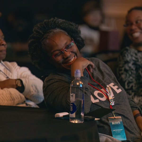 Three black women pictured laughting and smiling at a table.