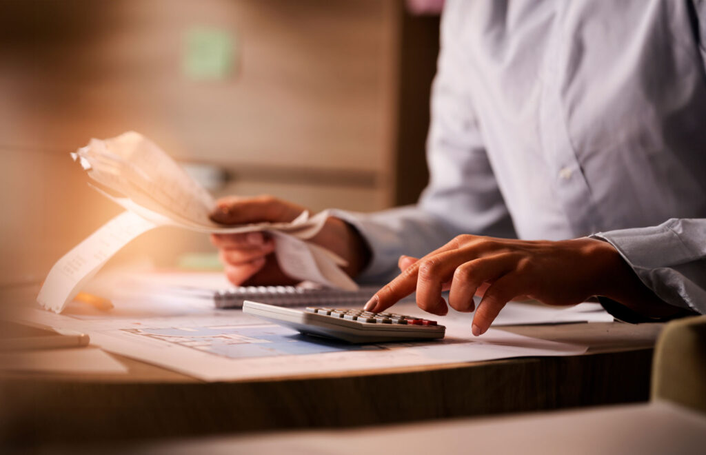 Hands of person using a calculator and holding financial receipts while sitting at a desk