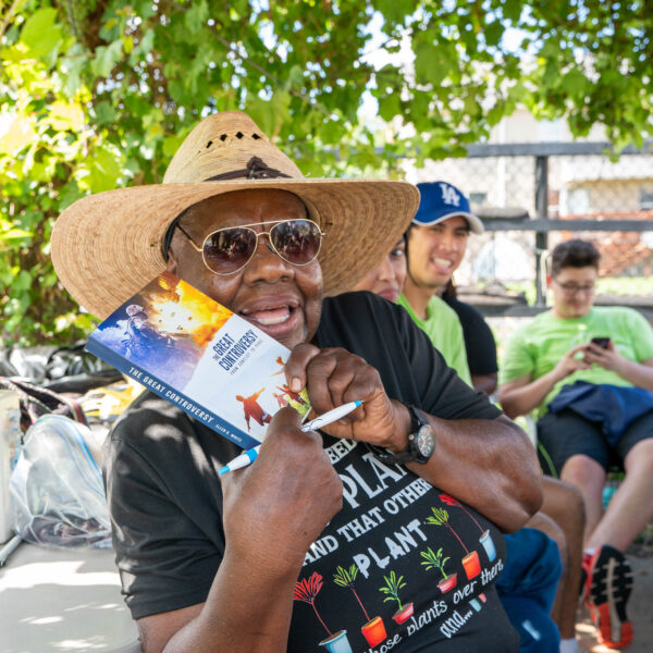A smiling woman wearing a wide-brimmed hat holds a copy of The Great Controversy.