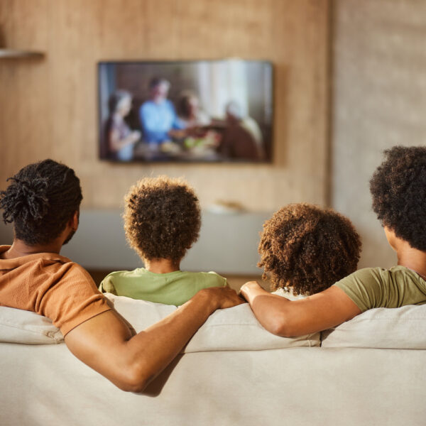 Back view of a black family watching TV at home.