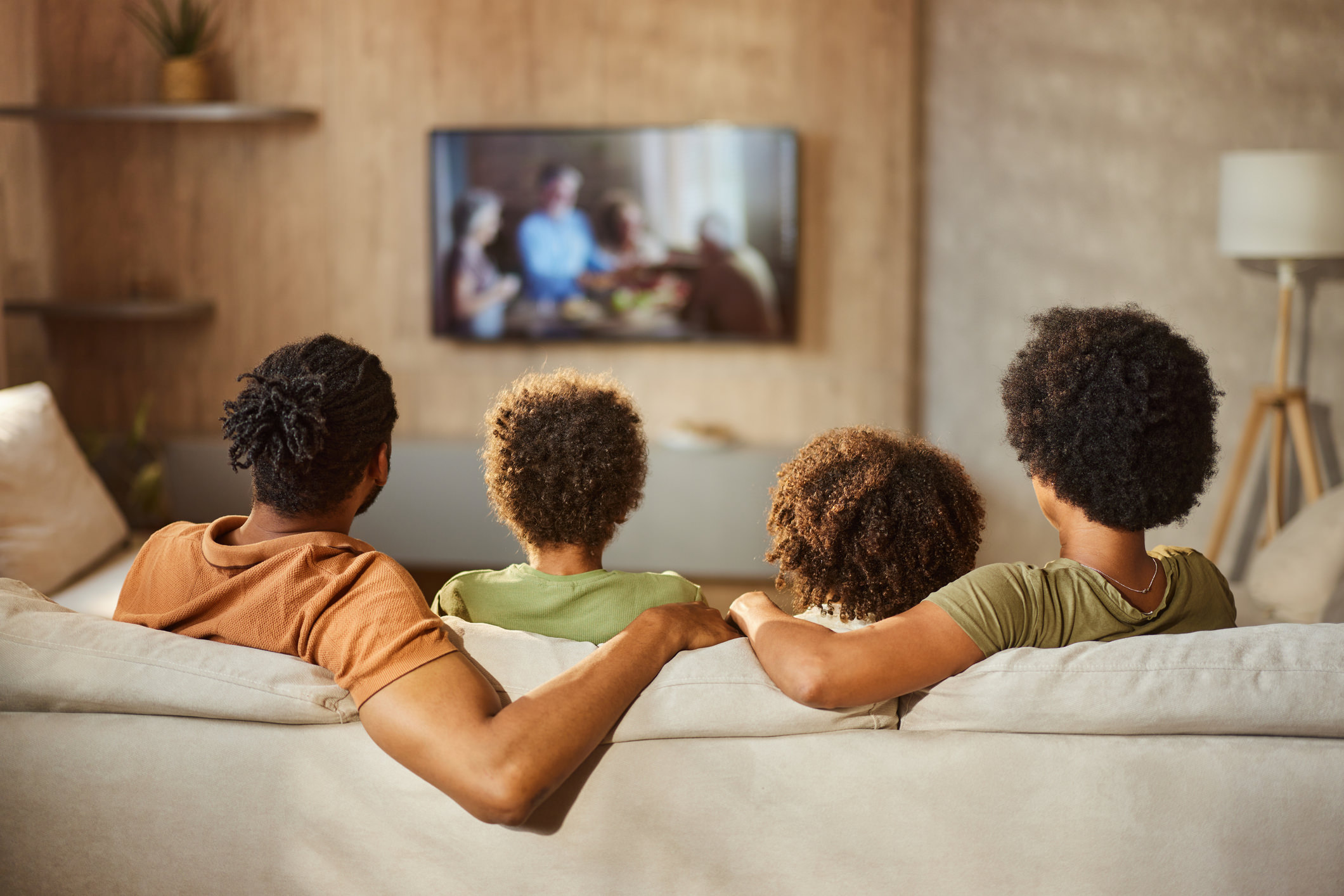 Back view of a black family watching TV at home.