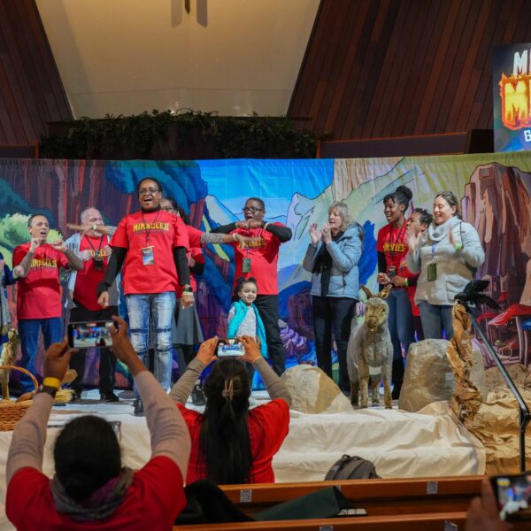 Group of adults onstage at a church in front of a colorful stage set for a children's Vacation Bible School.