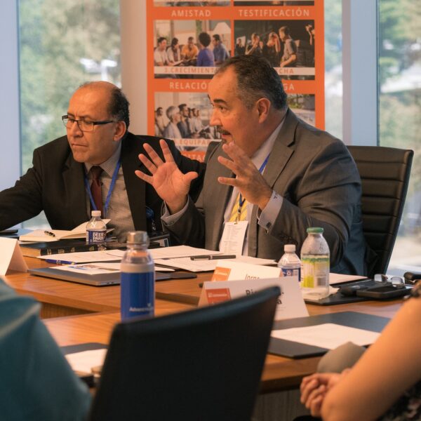 Group of people sitting around a conference table discussing ministry work. Sign in Spanish in the background.