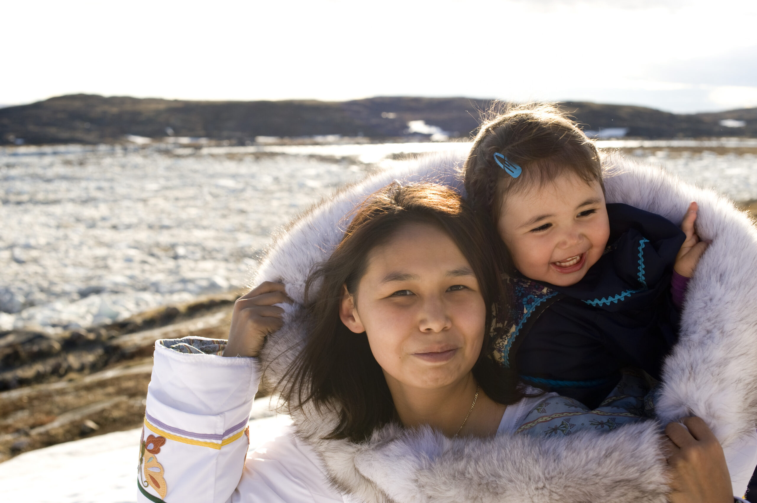 An Inuit mother has her daughter in her amouti, a traditional way to carry the young people. This is on the tundra of Baffin Island, Nunavut, Canada in late spring.