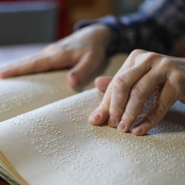 Photo showing two hands of a person who is reading braille type in a book.