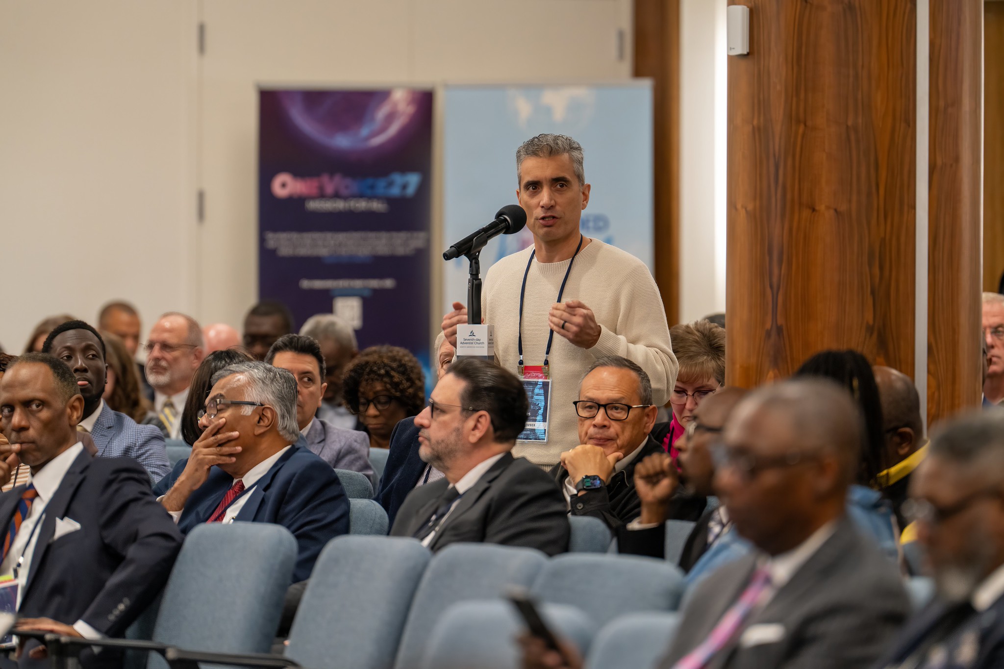 Man in the audience of a corporate meeting stands at a microphone to speak to the other attendees.