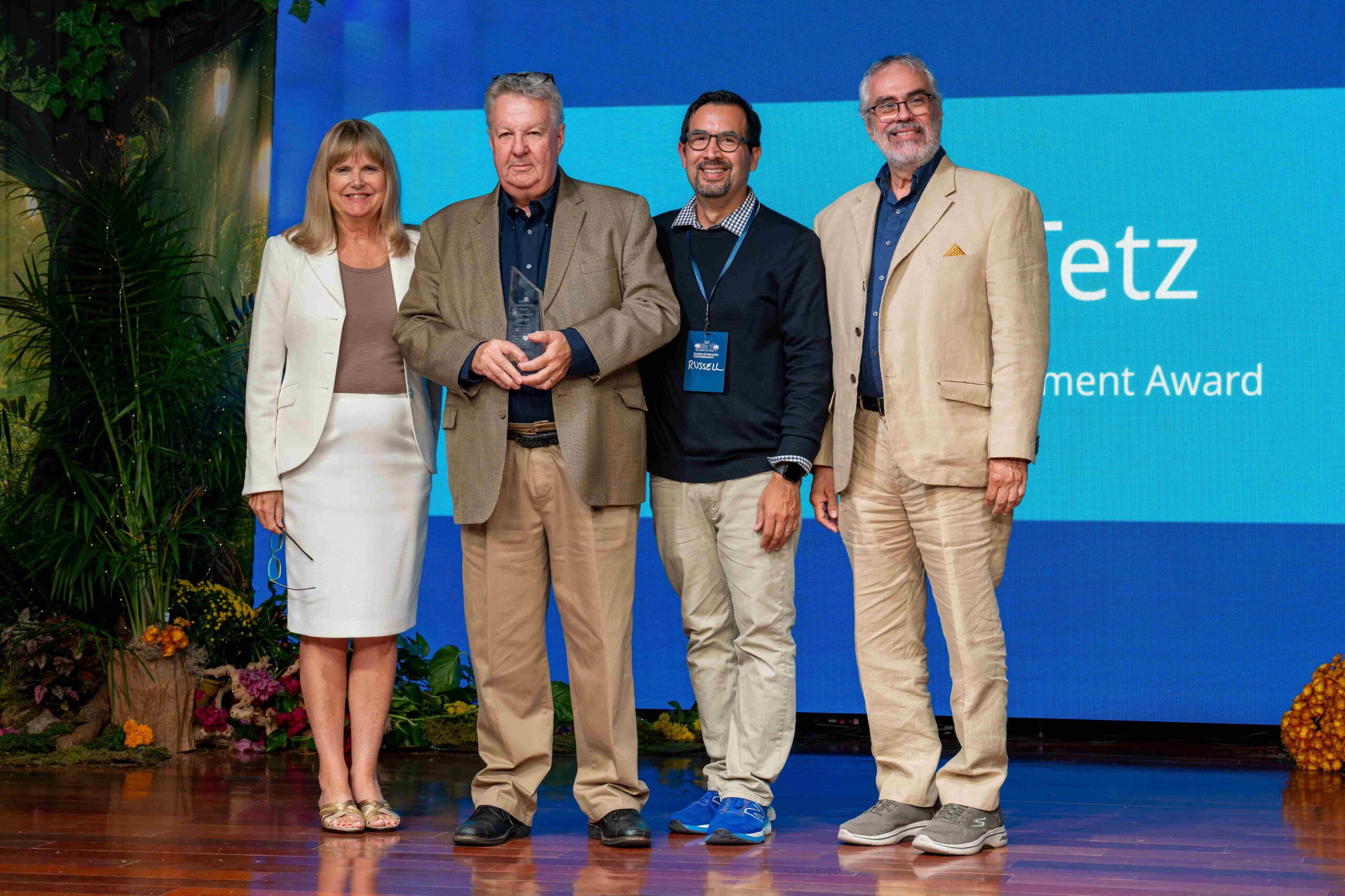 One women and four men stand on a stage. One of the men is holding an award.
