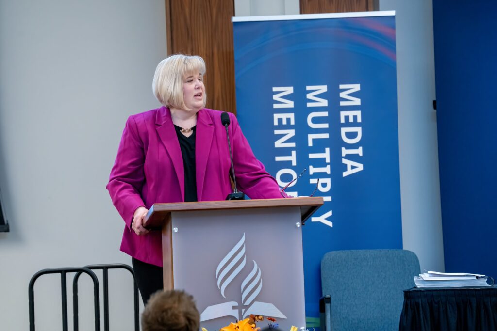 Middle age Caucasian woman stands at podium inside the North American Division headquarters building