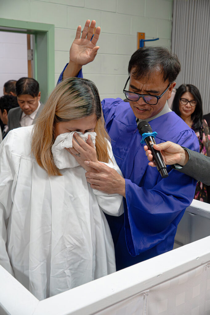 A man in a blue gown baptizes a woman in a white gown.