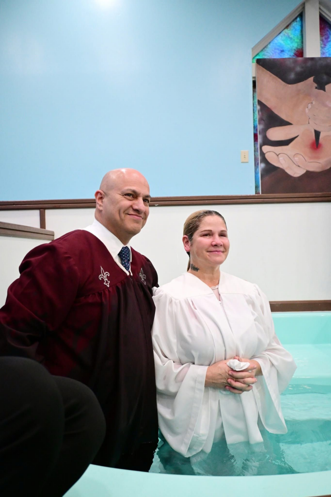 A smiling woman and male pastor stand in the baptismal pool