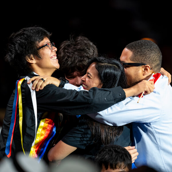 Two teen boys, an adult man and woman smile and hug on a stage