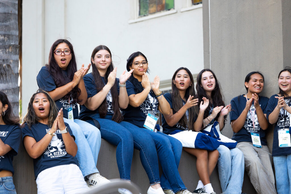 A group of women in blue La Sierra University t-shirts smile and clap.