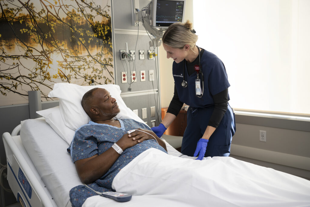 A male patient in a hospital room speaking with a healthcare professional.