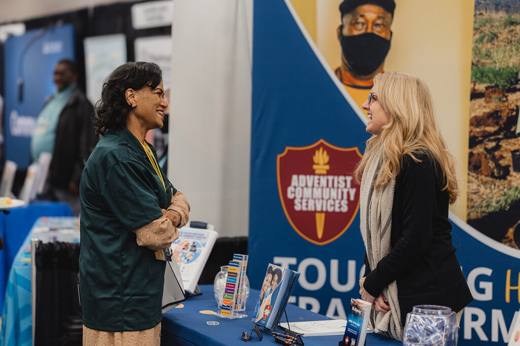 Two women smile while speaking at an exhibit booth