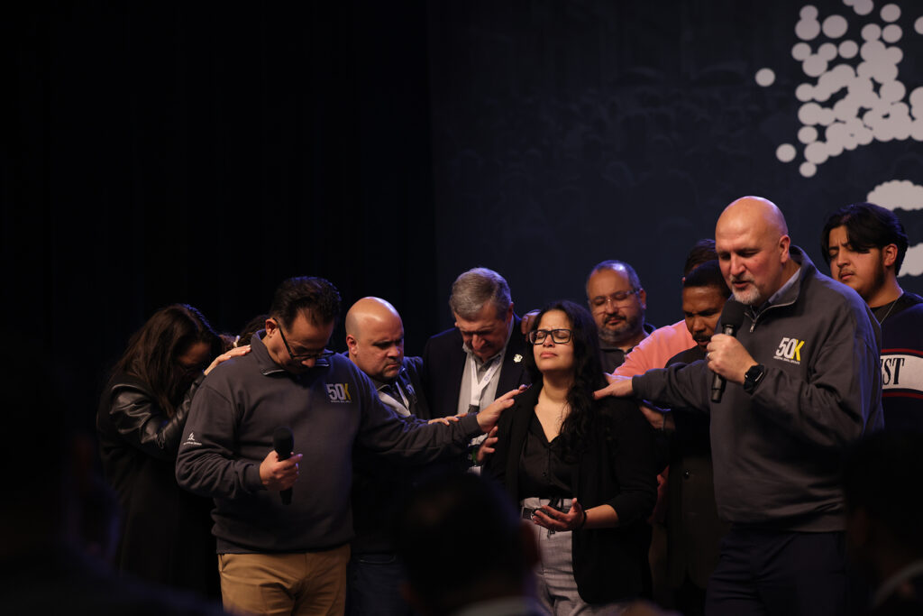 Photo of a group of men and women praying over a woman in the middle.