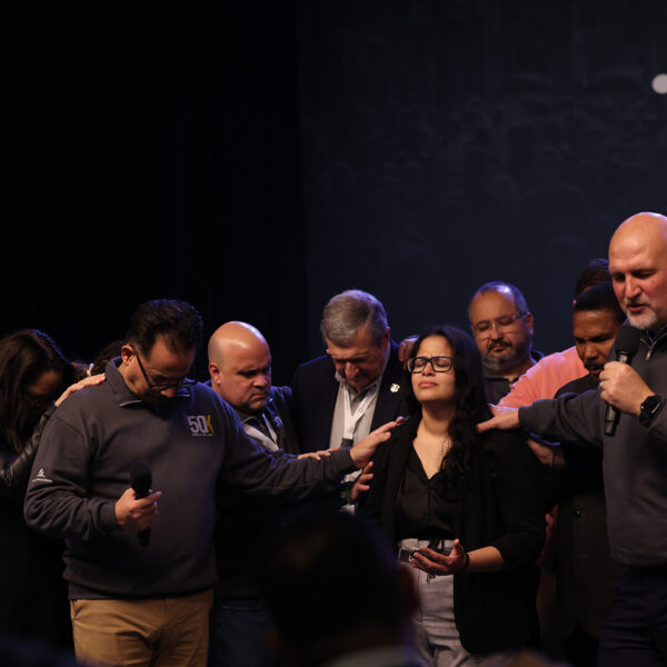 Photo of a group of men and women praying over a woman in the middle.