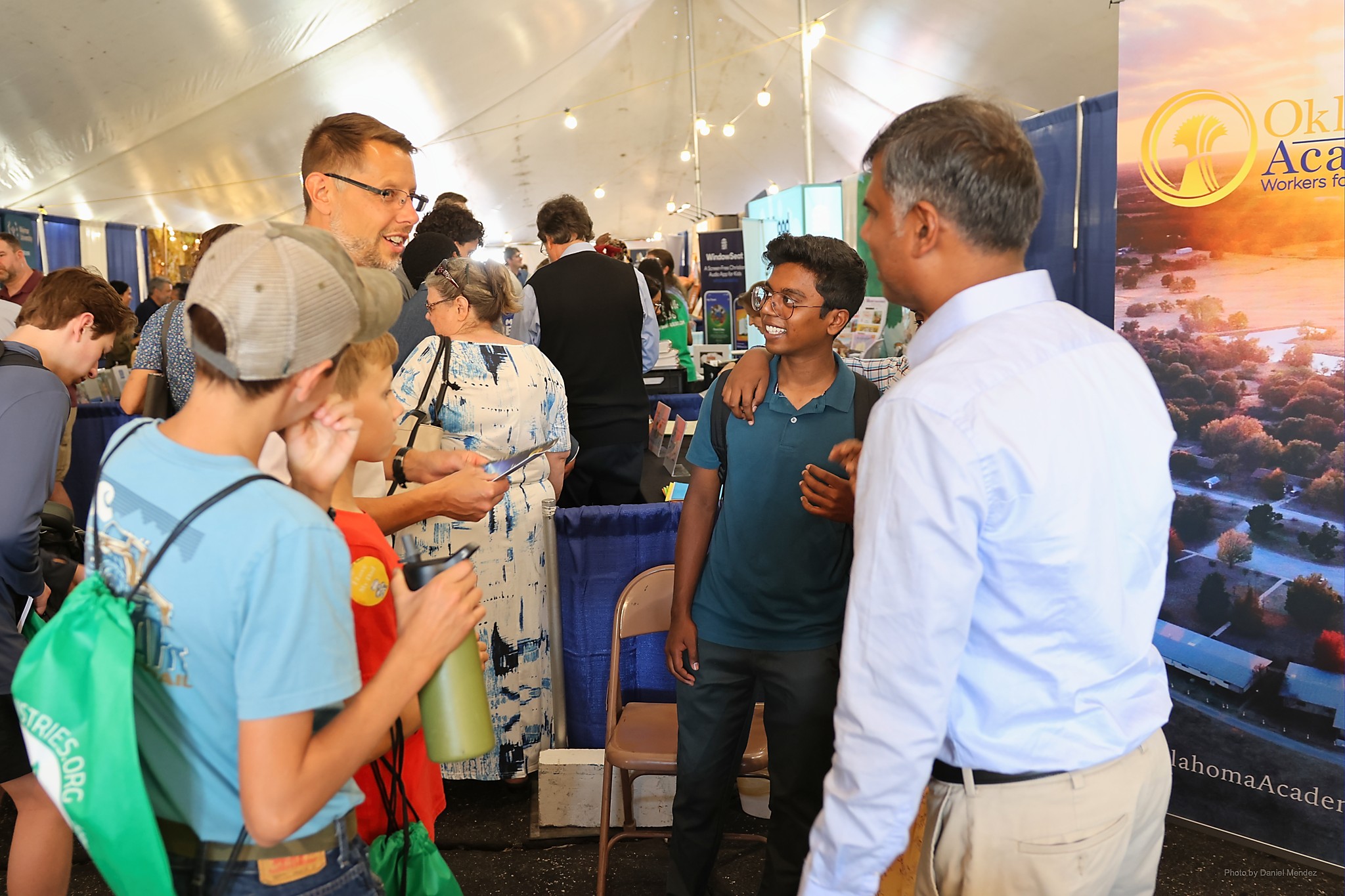 Group of people talking to each other inside a large meeting tent with exhibits.