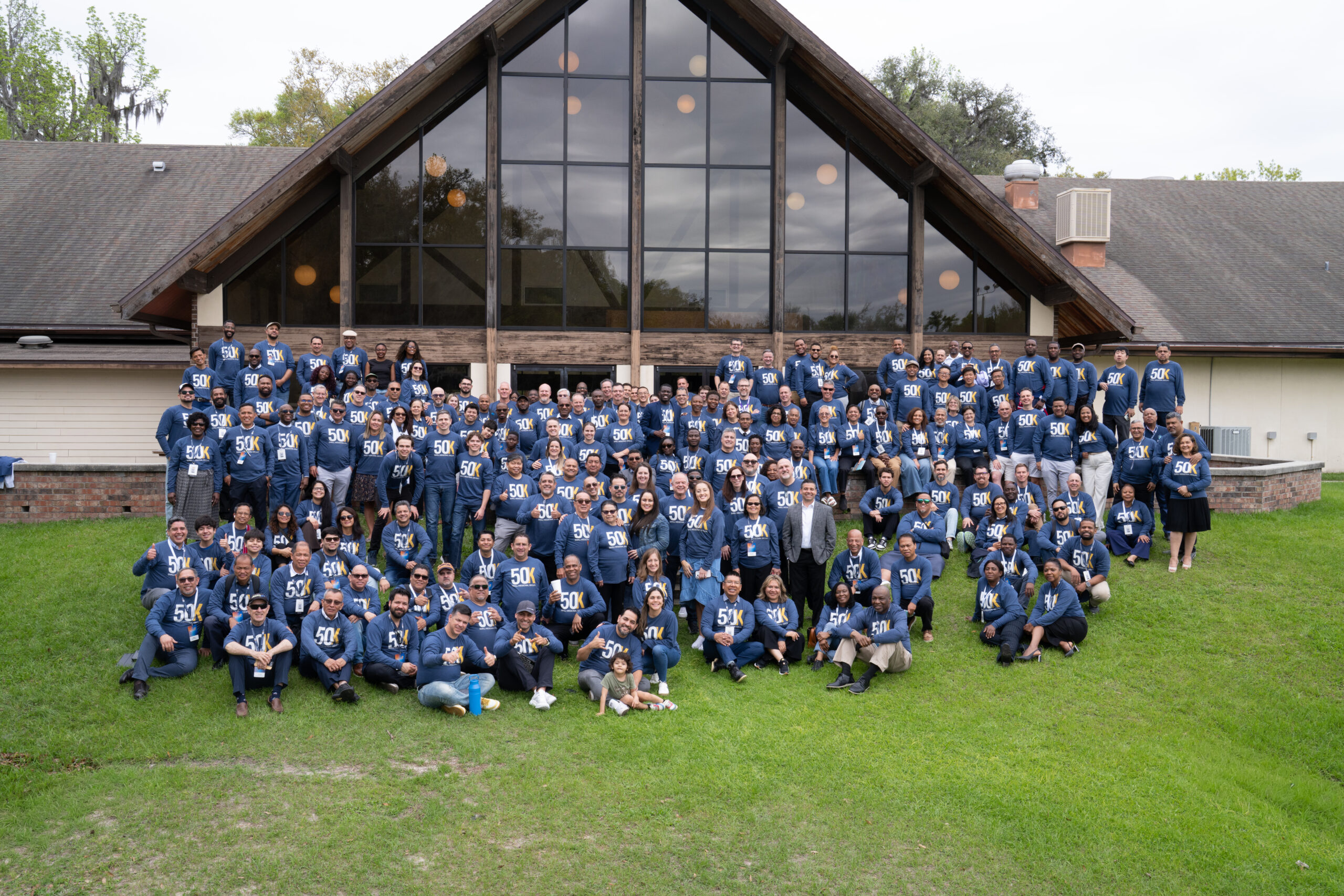 A group of participants in blue shirts gathers behind a building for a group photo.