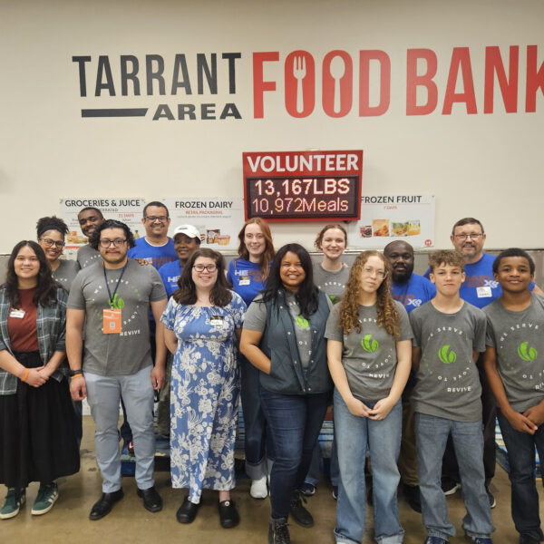 A diverse group of people smile for a photo in front of a wall that reads Tarrant Area Food Bank.
