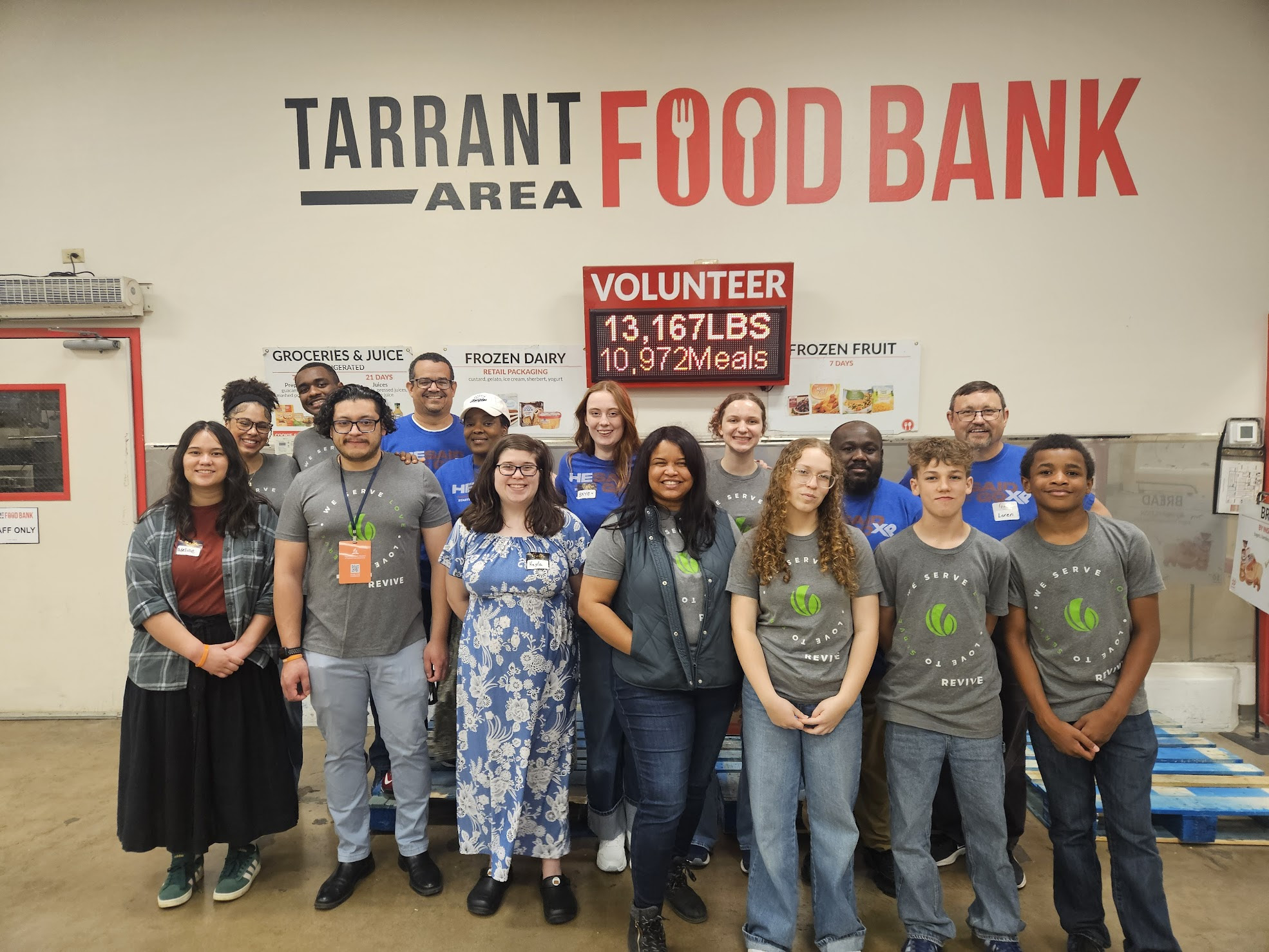 A diverse group of people smile for a photo in front of a wall that reads Tarrant Area Food Bank.