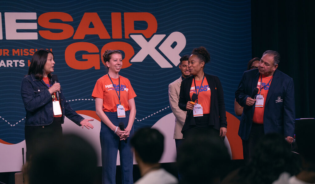 Three women and a man stand on stage. 