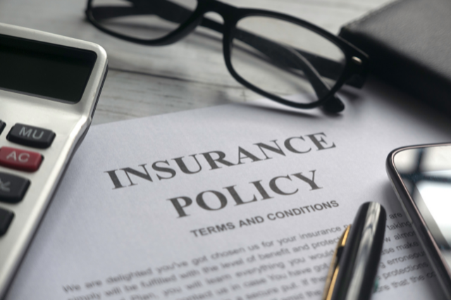 A paper that says insurance policy surrounded by items such as a calculator, pens, and glasses