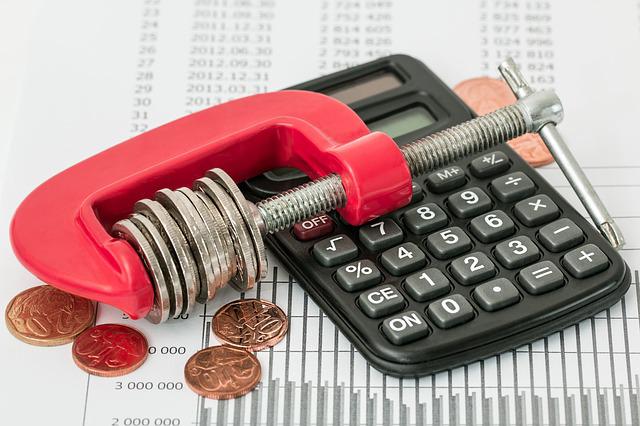 A calculator next to a red clamp squeezing coins