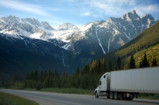 A white semi truck on a highway with white capped mountains