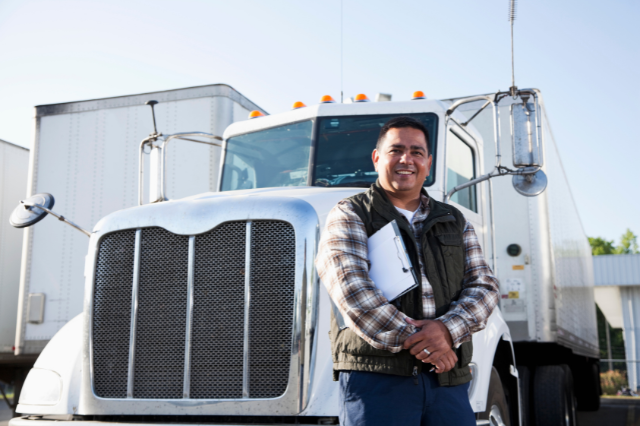 A man, smiling and leaning against a large truck