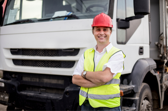 A truck driver in standing with his arms folded, smiling in front of a white truck. 