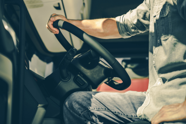 Close up of a person with one hand on the steering wheel of a big rig