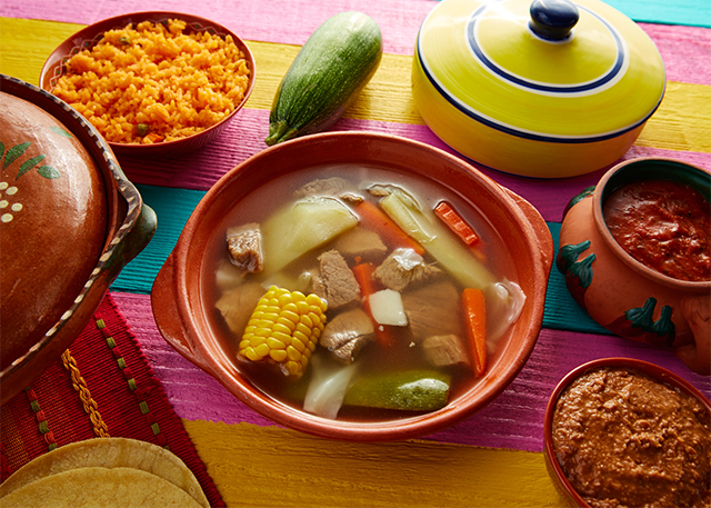 Image of caldo de res with fresh vegetables and other dishes surrounding it