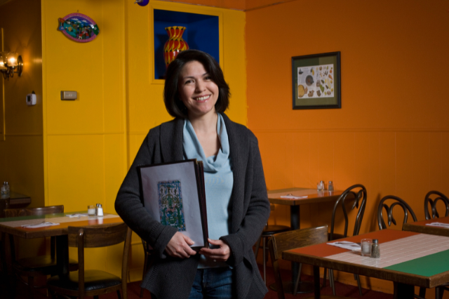 A woman restaurant owner holding menus in a brightly colored restaurant