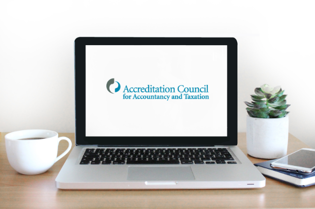 A laptop, with the Accreditation Council for Accountancy and Taxation logo on the screen, sitting on a wooden desk, along with a coffee cup, smart phone, notebook, and succulent.