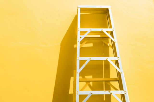 A white ladder leaned up against a blank yellow all