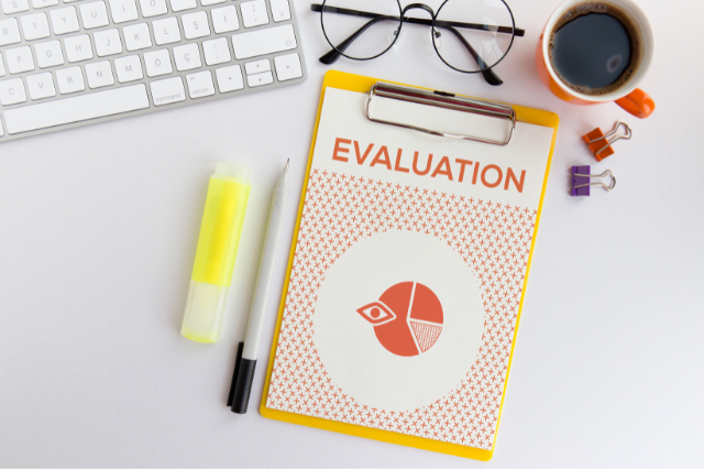  A clipboard that says Evaluation on it surrounded by various office items on a desk.