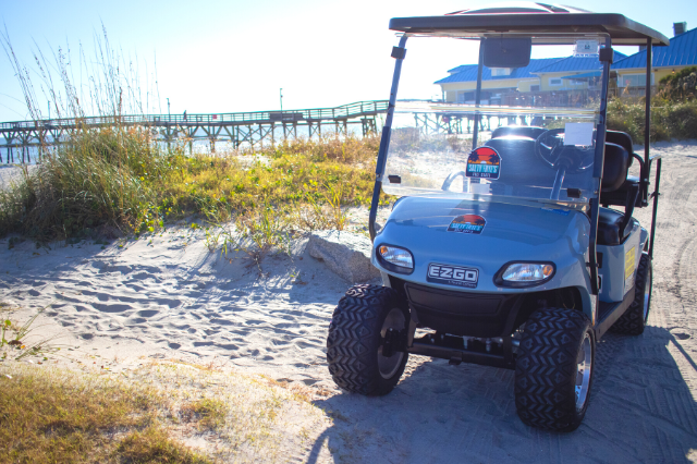 A Salty Frye's golf cart on the beach in front of a pier