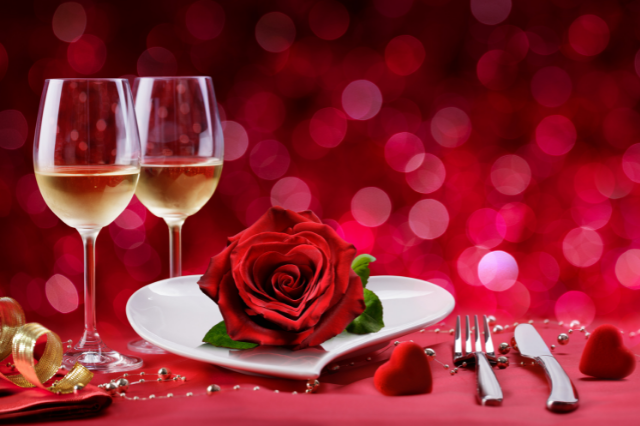 Wine glasses, a plate with a rose on it, and silverware on a table decorated for Valentine's Day
