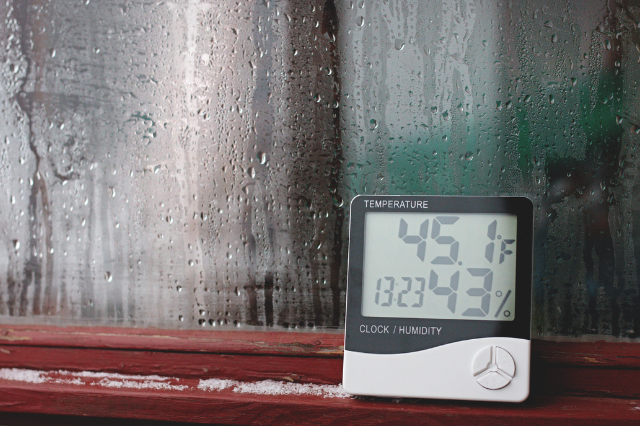 A thermostat in front of a window with condensation on the window