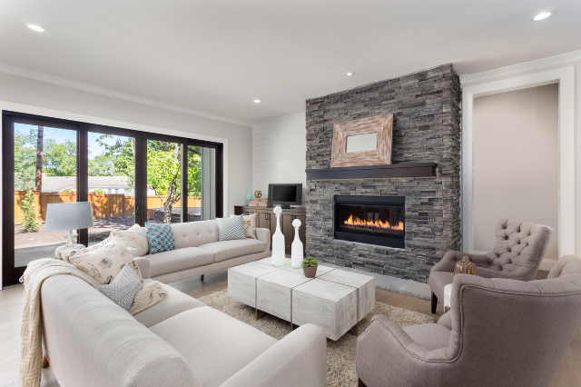 A bright living room with lots of natural lighting and white couches and a grey brick fireplace.