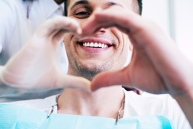 A man has his hands shaped like a heart in front of his beautiful teeth.